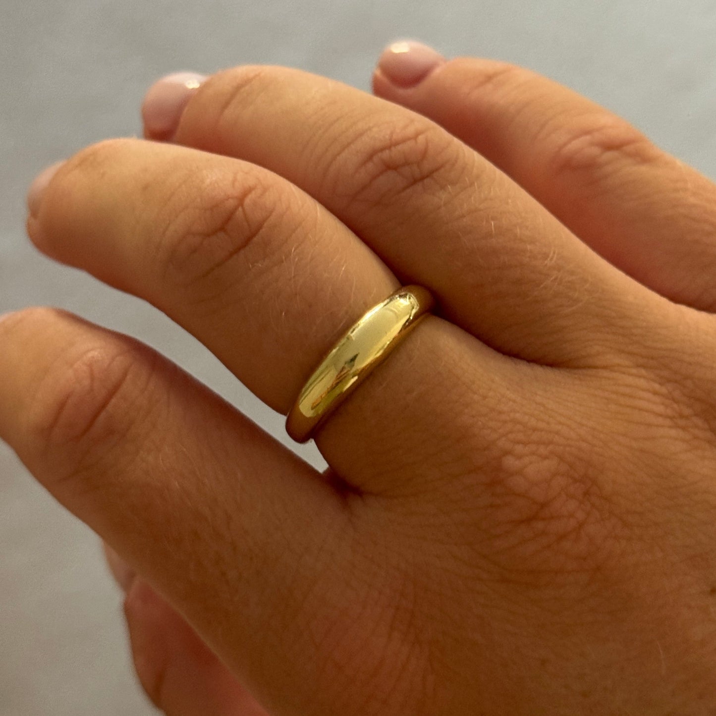 Hand wearing a gold ring on a neutral background