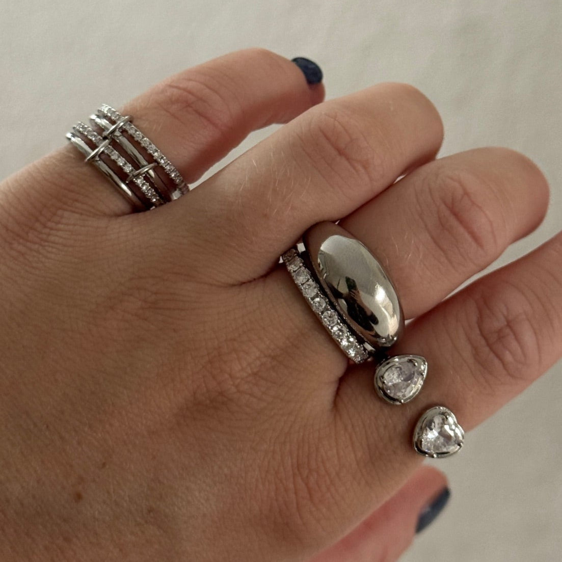 Hand wearing multiple silver rings on a plain background
