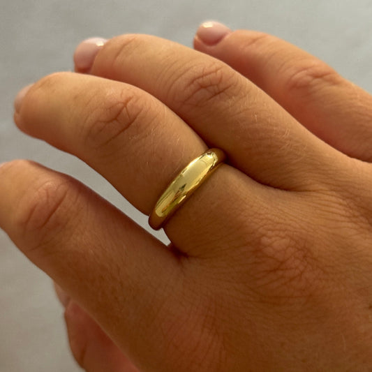 Hand wearing a gold ring on a neutral background