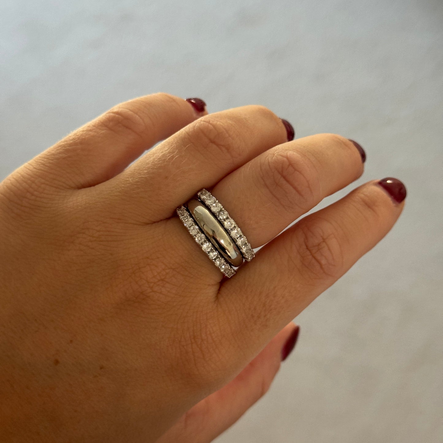 Hand wearing two silver rings on a plain background