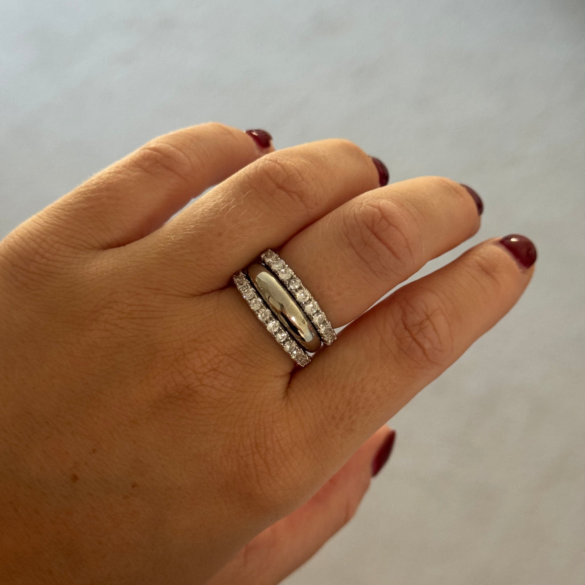 Hand wearing two silver rings on a plain background