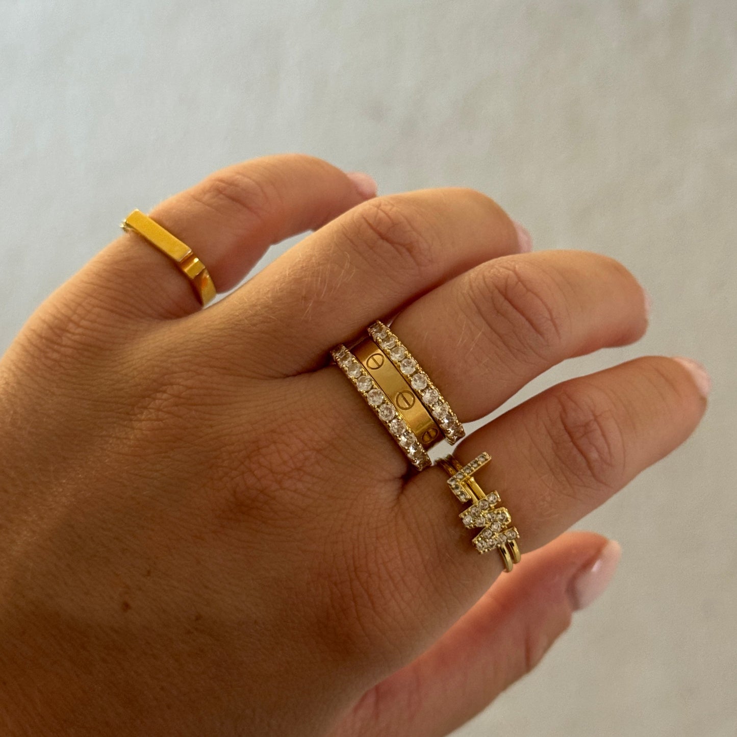 Hand wearing multiple gold rings on a neutral background