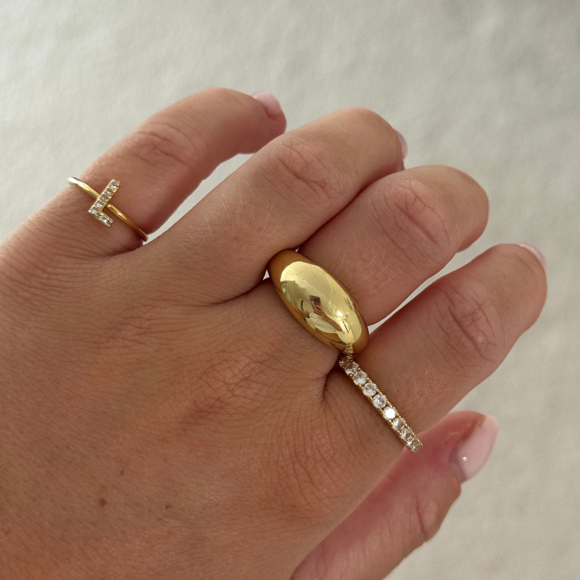 Hand wearing gold and diamond rings on a neutral background