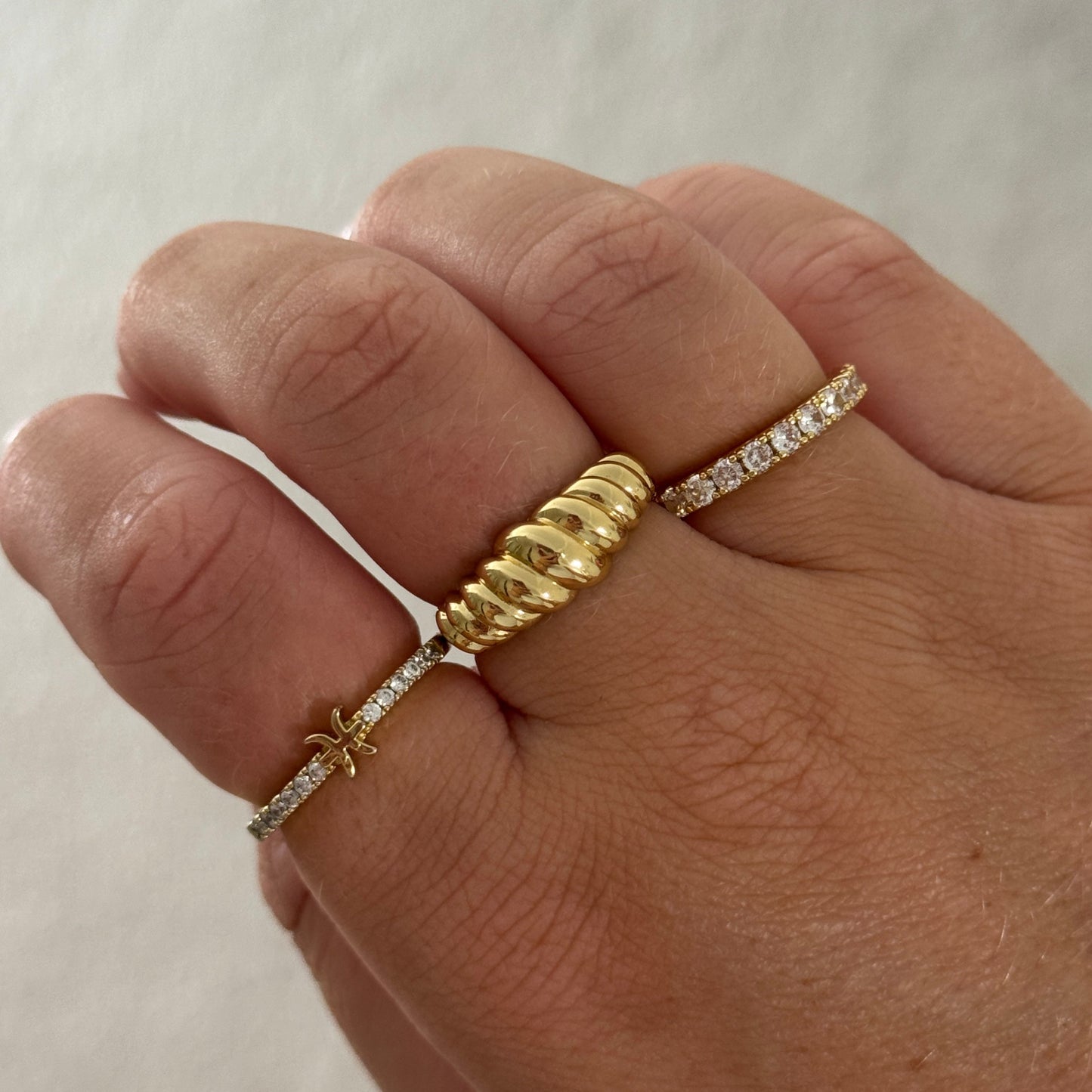 Hand wearing multiple gold rings with diamond accents on a neutral background