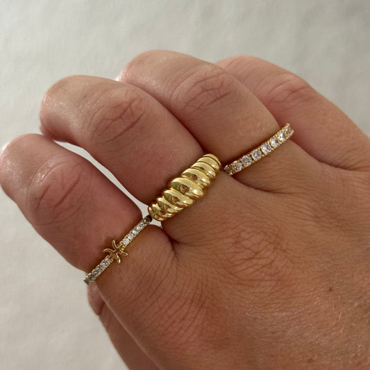 Hand wearing multiple gold rings with diamond accents on a neutral background