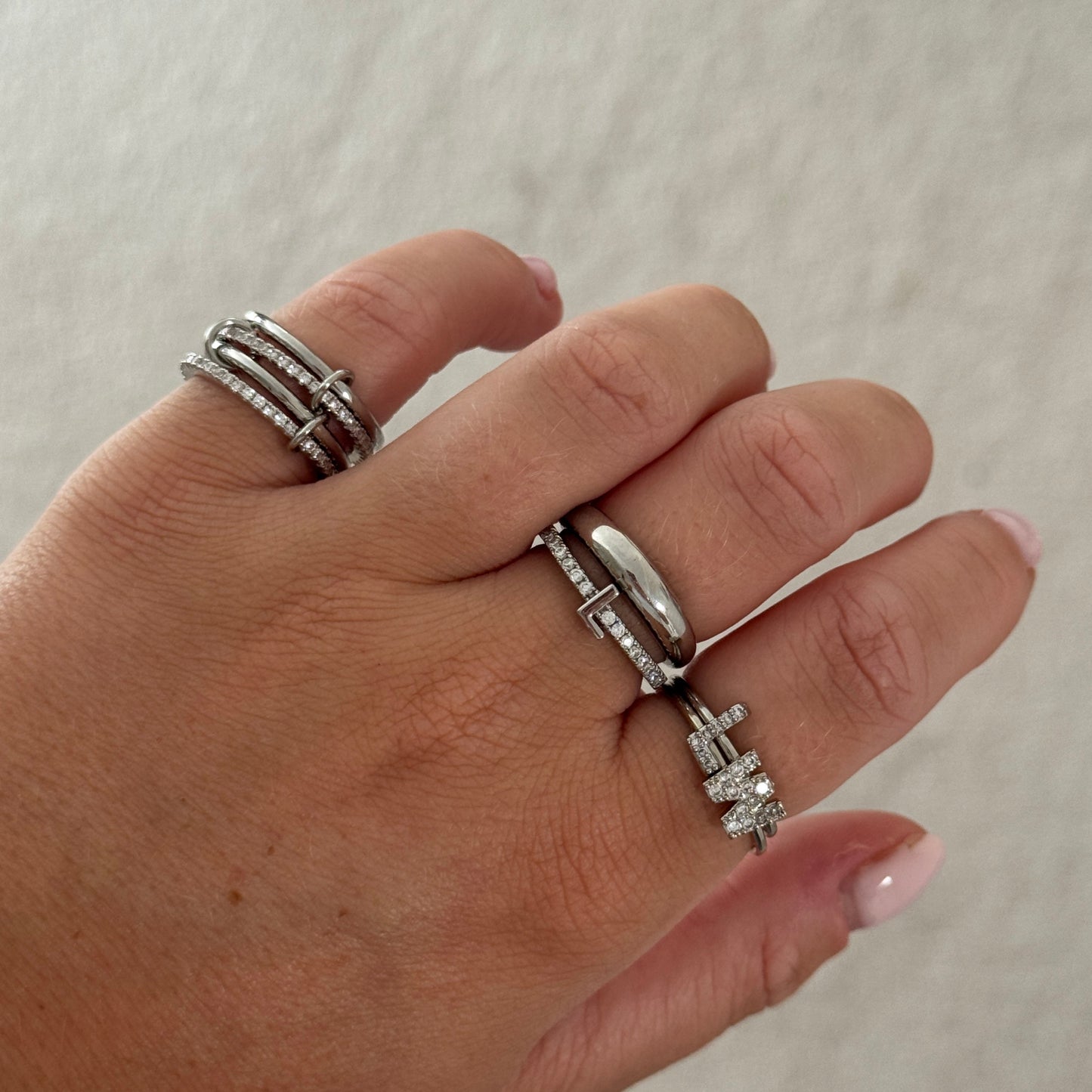 Hand wearing multiple silver rings on a light background