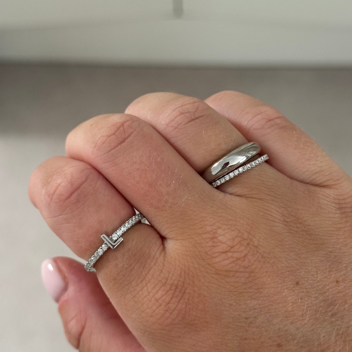 Close-up of a hand wearing two silver rings on a neutral background